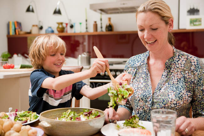 Son helping to serve salad for mother at the family dinner table — Stock Photo