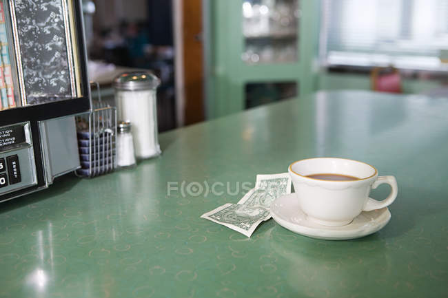 Taza de café y dinero en la mesa en la cafetería - foto de stock