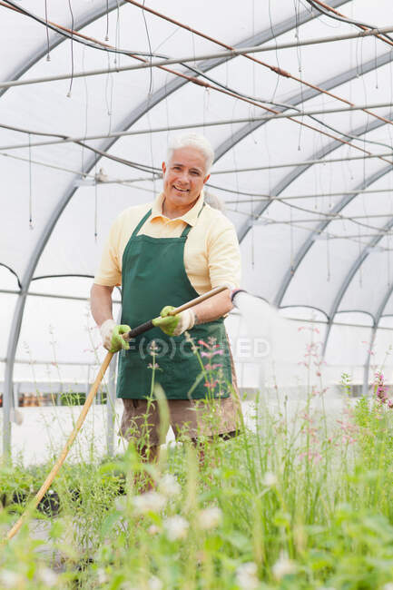 Senior homem plantas de rega no centro de jardim — Fotografia de Stock
