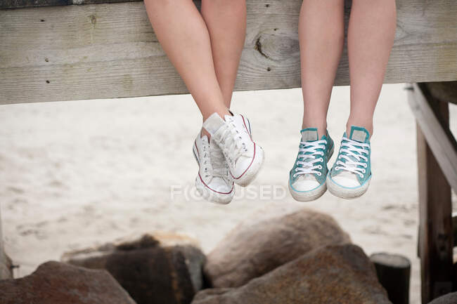 Young women sitting on pier on beach, low section — Stock Photo