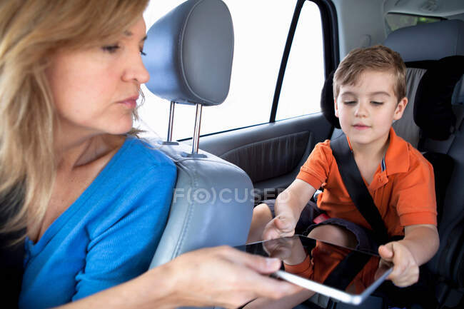 Mother passing digital tablet to son in back seat of car — Stock Photo