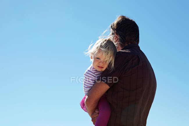 Зрілий чоловік тримає дочку в руках на блакитному небі — стокове фото