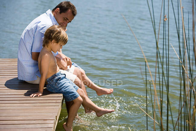 Padre e hijos en un muelle de madera - foto de stock