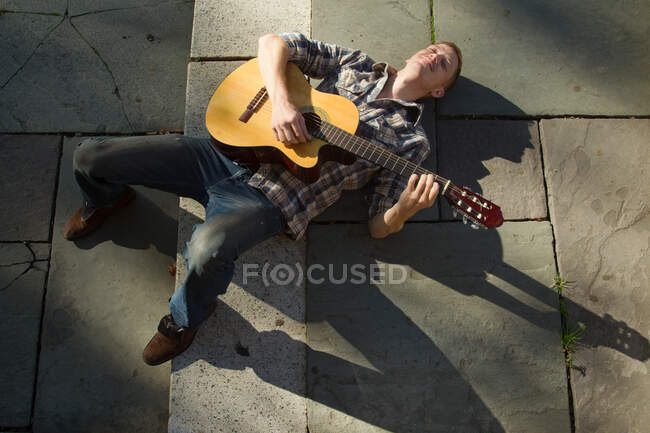Hombre adulto medio tocando la guitarra en tierra - foto de stock