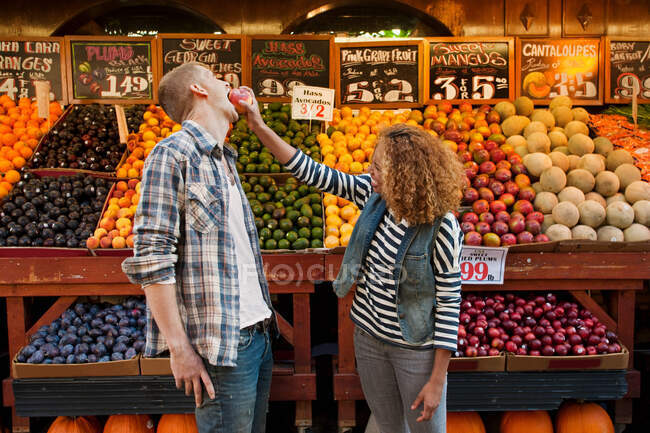 Young woman pushing apple into man's face — Stock Photo