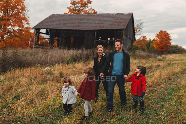 Средняя взрослая семья с тремя дочерьми, держащимися за руки и прогуливающимися по сельской местности — стоковое фото