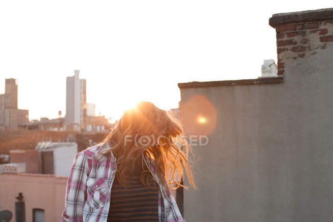 Young woman shaking hair on city rooftop — Stock Photo