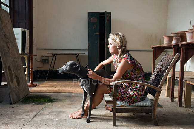 Junge Frau sitzt mit Hund auf Stuhl — Stockfoto
