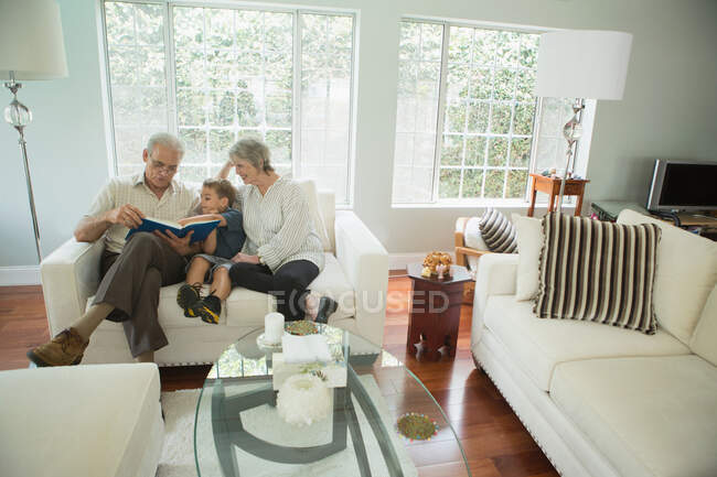 Avós mostrando menino álbum de fotos no sofá — Fotografia de Stock