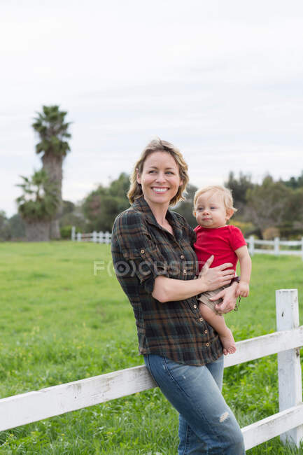 Woman holding son by wooden fence — Stock Photo