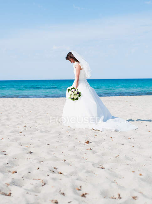 Mariée sur la plage tenant bouquet nuptial — Photo de stock