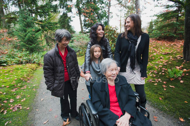 Семья из нескольких поколений толкает пожилую женщину в инвалидном кресле — стоковое фото