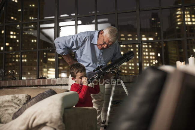 Abuelo enseñando a su nieto a usar el telescopio en casa - foto de stock
