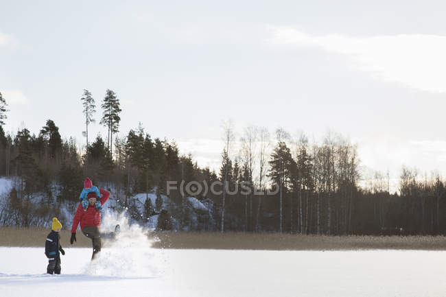 Pai e dois filhos brincando, correndo pela paisagem coberta de neve — Fotografia de Stock