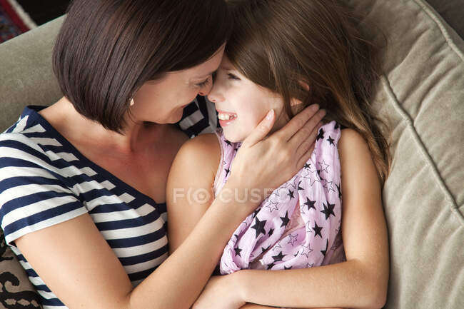 Mulher adulta média abraçando filha no sofá — Fotografia de Stock
