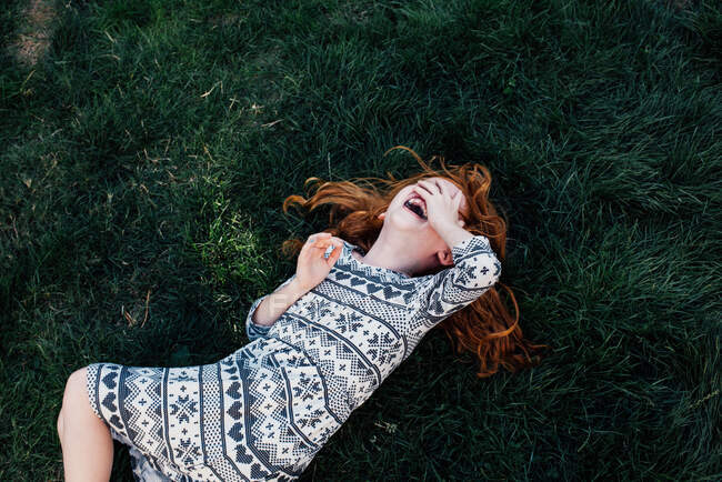 Vista de gran angular de la niña acostada en la hierba que cubre las risas de la cara - foto de stock