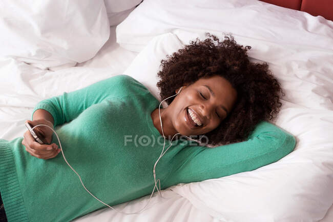 Woman listening to earphones on bed — Stock Photo
