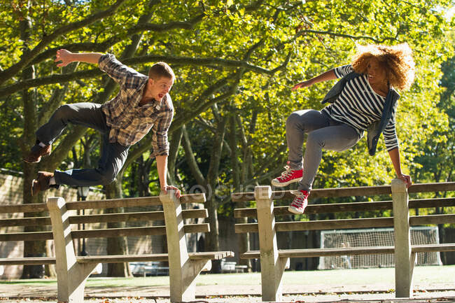 Couple leaping over park benches — Stock Photo