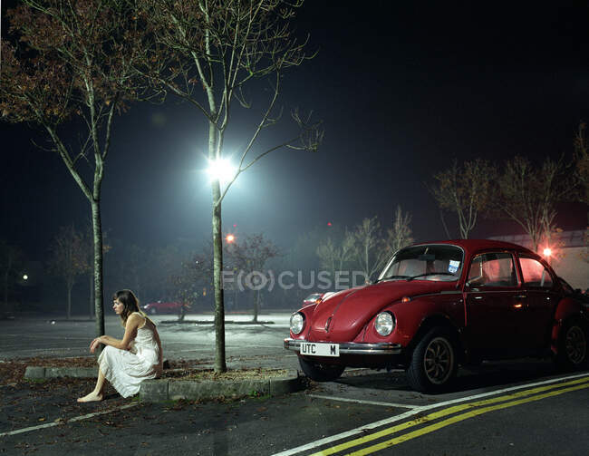 Mulher sentada no parque de estacionamento à noite — Fotografia de Stock