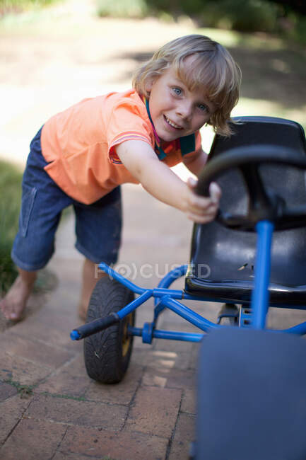 Boy pushing go kart outdoors — Stock Photo