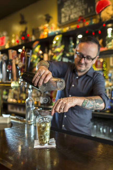 Barman pouring cocktail into glass at public house counter — Stock Photo