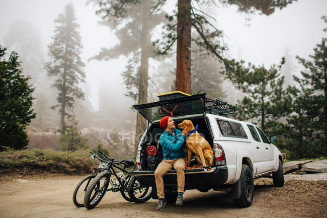 Man and dog sitting on tailgate of off road vehicle, Sequoia National Park, California, USA — Stock Photo