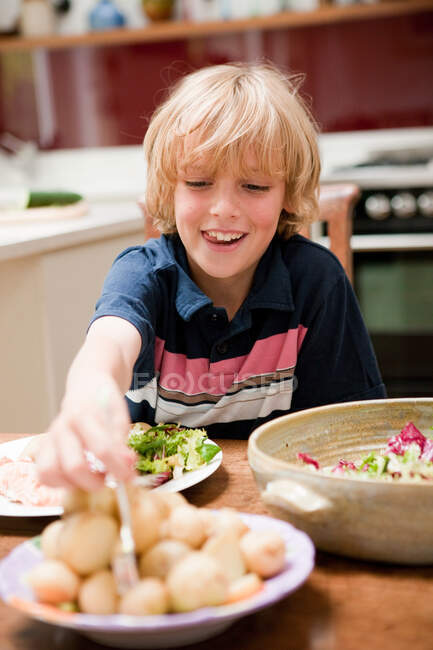 Kleiner Junge am Esstisch der Familie hilft sich mit Kartoffeln — Stockfoto
