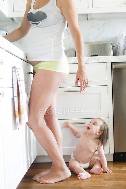 Baby girl on kitchen floor by pregnant mother — Stock Photo