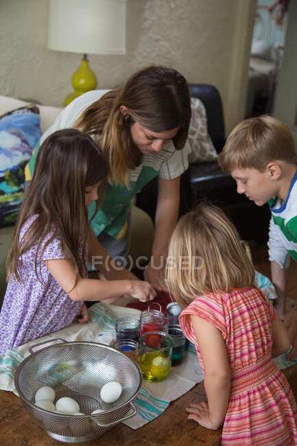 Mãe e três crianças tingindo ovos de Páscoa na mesa — Fotografia de Stock