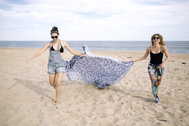 Mujeres arrastrando manta de picnic en la playa, Amagansett, Nueva York, Estados Unidos - foto de stock