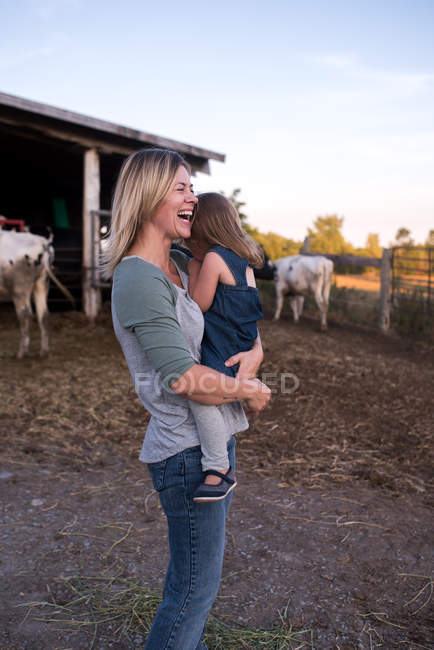 Madre llevando hija en la granja, madre riendo - foto de stock