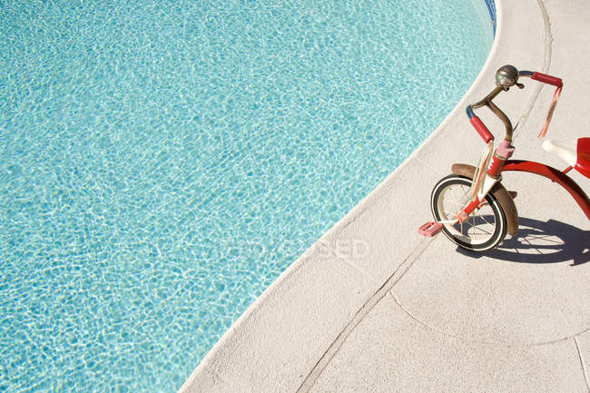 Child tricycle at edge of swimming pool — Stock Photo