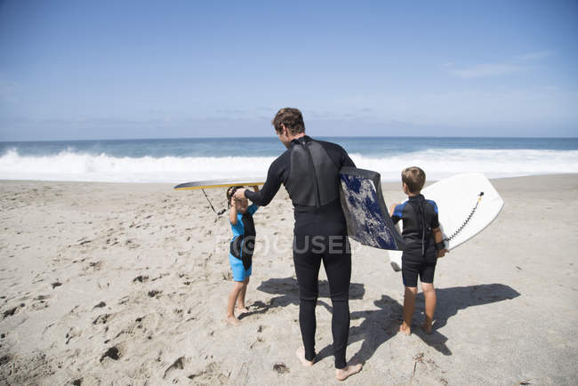 Vista trasera del padre y dos hijos que se preparan para el bodyboarding en la playa, Laguna Beach, California, EE.UU. - foto de stock