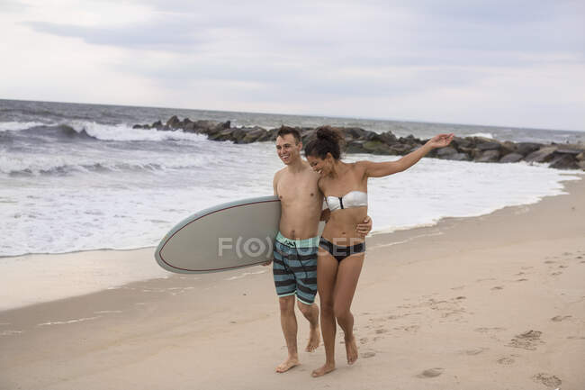 Romántica pareja de jóvenes surfistas paseando por Rockaway Beach, Estado de Nueva York, Estados Unidos - foto de stock