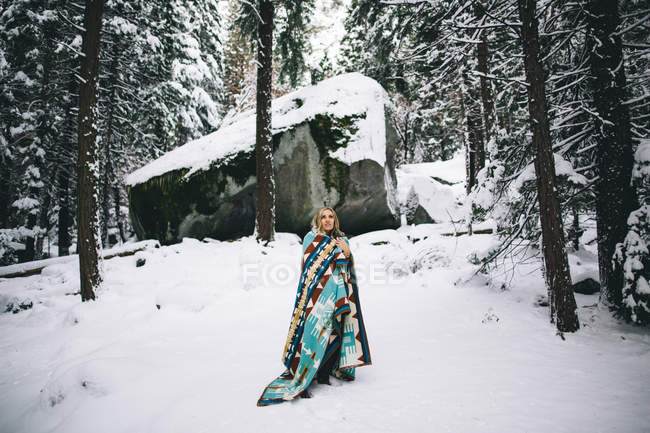 Woman in snow-covered forest wrapped in blanket — Stock Photo