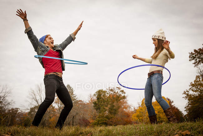 Pareja joven jugando con aros de plástico en el parque de otoño - foto de stock