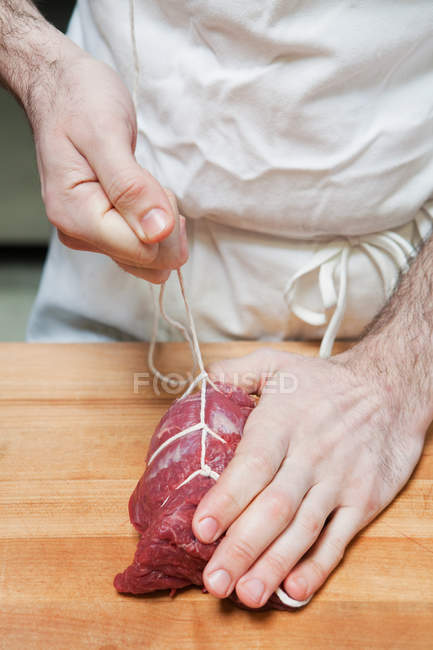 М'ясника, пов'язуючи яловичини вирізка з рядка — стокове фото