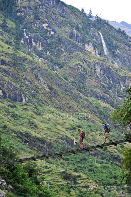 Trekkers cruzan un puente colgante de 60 metros de largo, al norte de Tal, Bhulbhule, Nepal - foto de stock