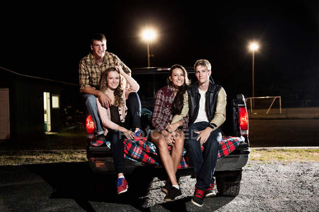 Retrato de amigos sentados na bagageira do carro à noite — Fotografia de Stock