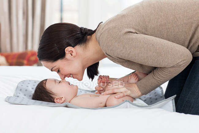 Mère frottant nez avec bébé garçon sur matelas à langer — Photo de stock