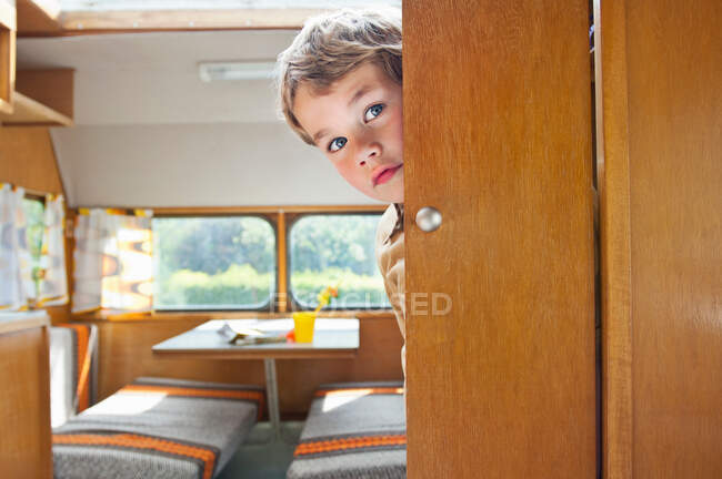 Menino espreitando porta redonda na caravana — Fotografia de Stock