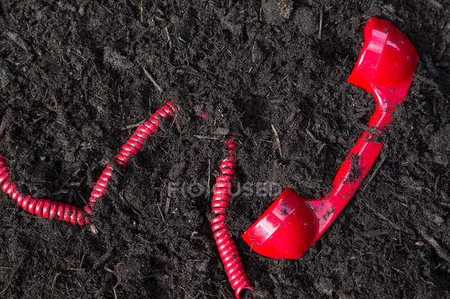 Red retro telephone handset buried in soil — Stock Photo