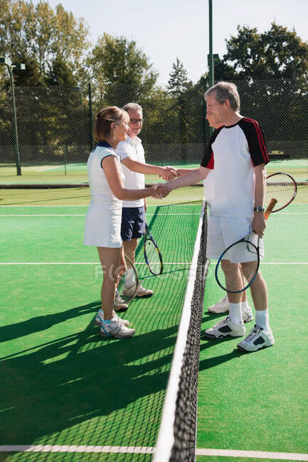 Взрослые пожимают руки на теннисном корте — стоковое фото