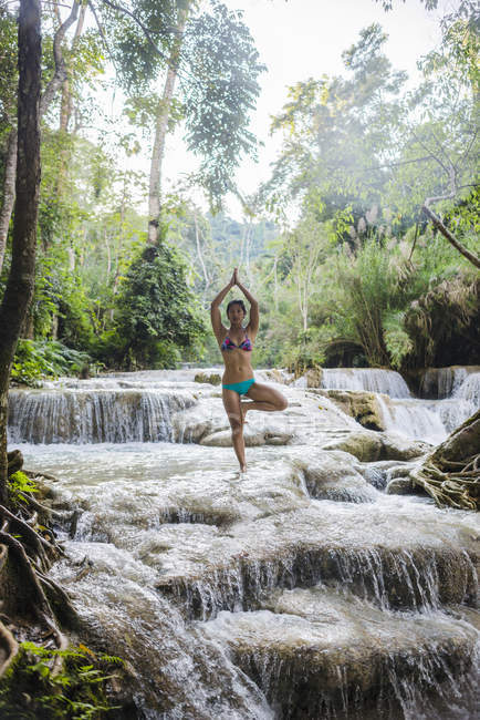 Frau steht auf einem Bein in Baumpose, im Kuang si Wasserfall, luang prabang, laos — Stockfoto