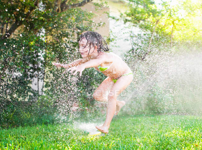Menina jogando no aspersor de jardim no verão — Fotografia de Stock