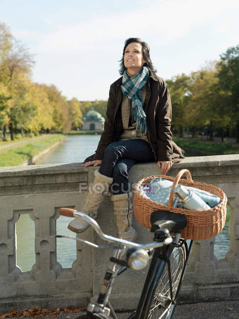 Mujer sentada en el puente del río en otoño - foto de stock