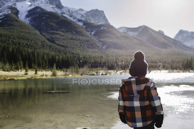 Jeune garçon au bord de la rivière, vue arrière, Trois Sœurs, Montagnes Rocheuses, Canmore, Alberta, Canada — Photo de stock