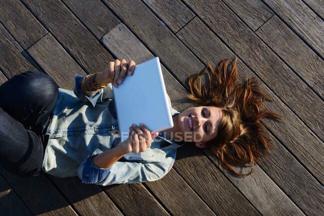 Jovem deitada em tábuas de madeira segurando tablet digital — Fotografia de Stock
