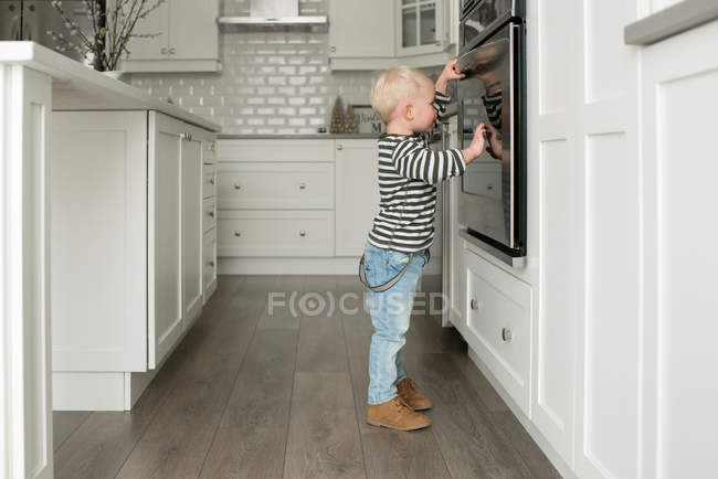 Мальчик на кухне, смотрит в духовку — стоковое фото