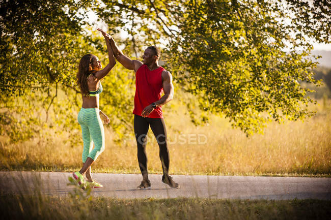 Jovem casal correndo dando altos cinco no parque — Fotografia de Stock